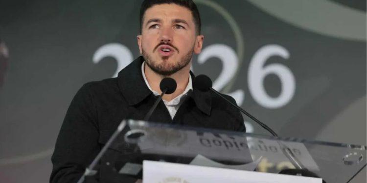 Man Speaking at a Podium with Two Microphones During a Formal Event, Blurred Backdrop Showing 2026 Behind Him. | La Silla Regia