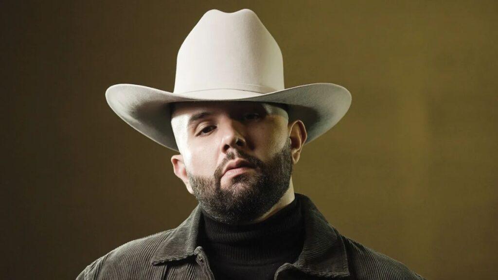 Portrait of a Man Wearing a White Cowboy Hat and Dark Jacket Against a Brown Backdrop. | La Silla Regia
