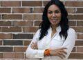 Woman with Long Dark Hair in a White Button-down Shirt, Smiling with Arms Crossed in Front of a Brick Wall. | La Silla Regia