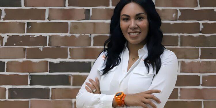 Woman with Long Dark Hair in a White Button-down Shirt, Smiling with Arms Crossed in Front of a Brick Wall. | La Silla Regia