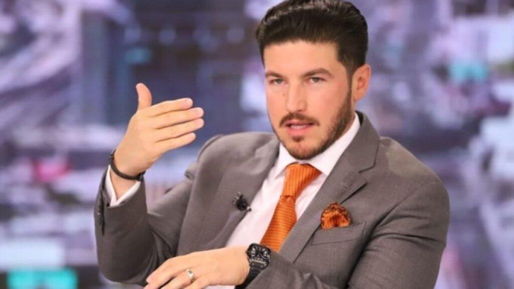 a Well-dressed Man in a Gray Suit and Orange Tie Speaks While Gesturing with His Right Hand on a Tv Set. | La Silla Regia