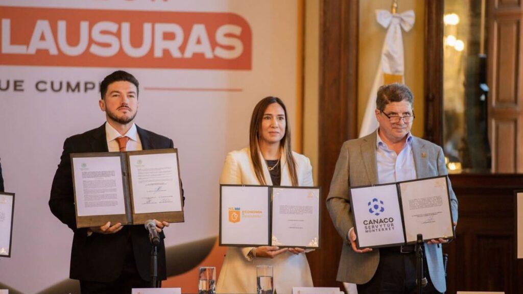 Three Professionals in Business Attire Stand at a Signing Ceremony, Each Holding Open Folders with Documents in Front of a Banner. | La Silla Regia